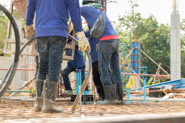 Workers put jeans on their feet holding concrete vibrators in their hands on rebar for pouring concrete in construction sites, columnar backgrounds and building conditions during construction.