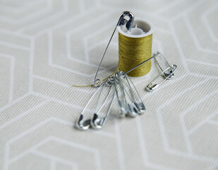 Tailor pins and spool of green thread on gray fabric