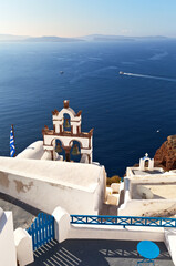 Fototapeta na wymiar Greece. Santorini island. Beautiful seascape with famoust Oia town with white Cycladic houses and traditional arched bell tower on sunny day. Narrow streets without tourists. Seaside background