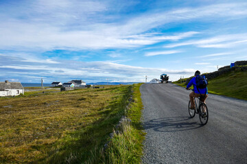 Beautiful Inis Oirr in the Aran Islands. Cyclist on road with cloudy blue sky and field with quaint housses.