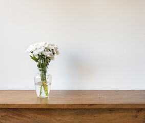 Close up of white chrysanthemums in glass vase on oak table against neutral background (selective focus)