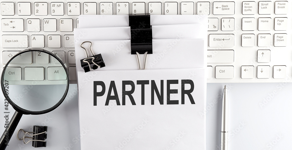 Poster words partner written on papers on a computer keyboard with magnifier and pen