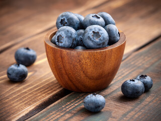Ripe blueberries placed in lumber bowl on wooden table in summer