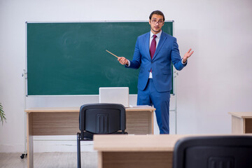 Young male teacher in suit in front of green board