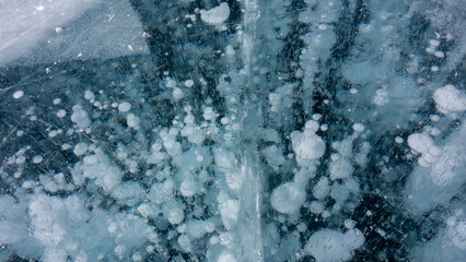 In the thickness of the transparent turquoise ice, white gas bubbles frozen in the form of columns...