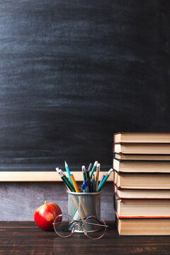 Concept to teacher's day. Pens, apple, pencils, books and glasses on the table, against the background of a chalkboard. Back to school, copy space.