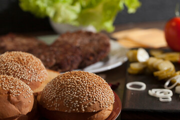Cooking burger, ready-made ingredients for cheeseburger on dark wooden board, out of focus background