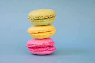 Pile of french green, yellow and pink round macarons with fillers on blue background  with copy space.French pastry