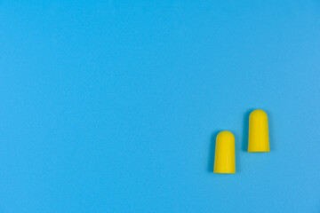 Two yellow earplugs on a blue background.