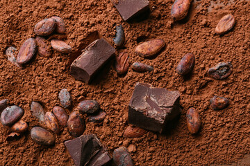 Heap of cacao powder with beans and chocolate pieces as background