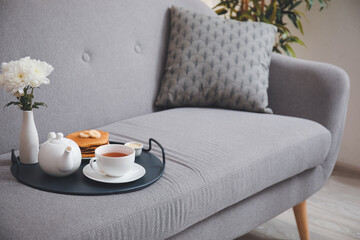 Tray with tasty breakfast and flowers on sofa in room