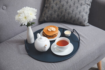 Tray with tasty breakfast and flowers on sofa in room