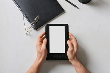 Male hands with e-reader, notebook and eyeglasses on light background