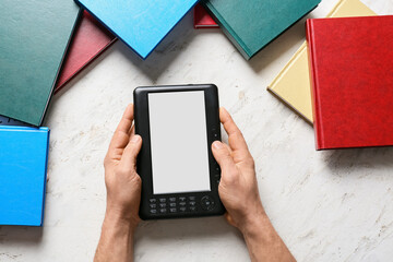 Male hands with e-reader and books on light background