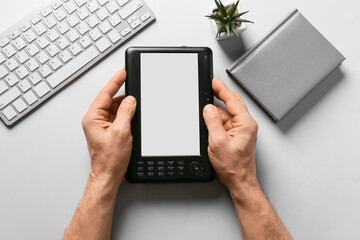 Male hands with e-reader, computer keyboard and book on light background