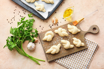 Board with uncooked garlic buns on color background