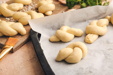 Baking sheet and board with uncooked garlic buns on color background
