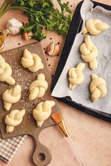 Baking sheet and board with uncooked garlic buns on color background