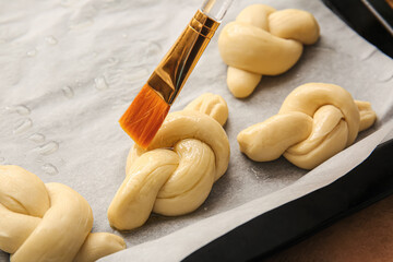 Greasing uncooked garlic buns with oil on color background, closeup