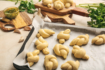 Baking sheet with uncooked garlic buns on light background