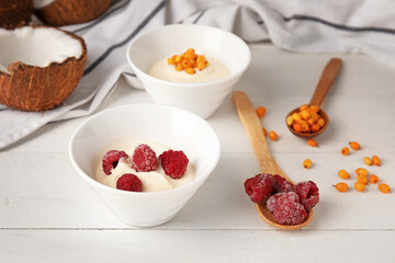 Bowls of tasty coconut yogurt on light wooden background
