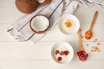 Bowls of tasty coconut yogurt on light wooden background