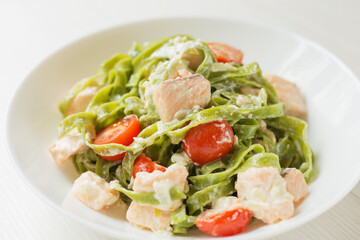 Pasta seafood. A close up view of a plate of spinach Tagliatelle with salmon in cream sauce on light table. Mediterranean cuisine.