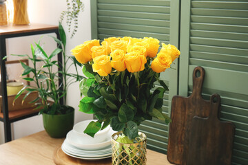 Vase with beautiful yellow roses on table in kitchen
