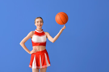 Beautiful young cheerleader with ball on color background