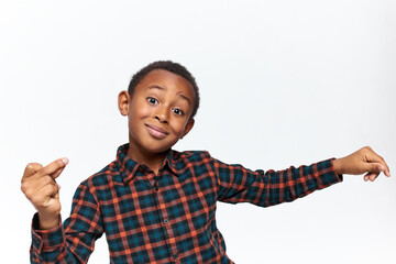 Studio image of handsome positive Afro American little boy in checkered shirt posing against white background making gesture, clicking fingers, producing snapping sound to keep rhythm. Body language