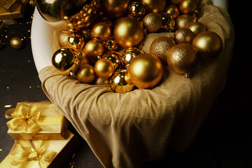 Golden Christmas balls of different sizes in a bath covered with a cloth, there are gifts in gold packaging next to them.