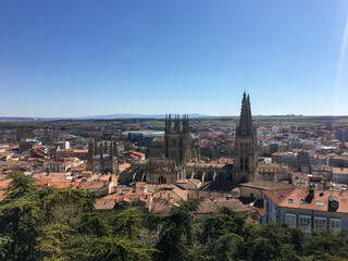 Fototapeta premium Panoramic view of Burgos with its famous cathedral surrounded by buildings in the foreground and agricultural fields and mountains in the background, on the horizon.