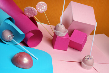 Pink chocolate cake pops on sticks are on a background with bright shapes from paper