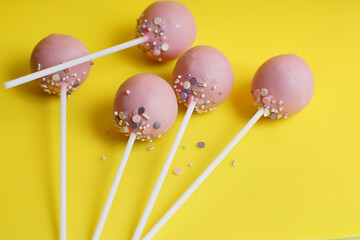 Delicate pink cake pops on long sticks lie on a yellow paper background