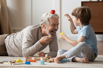 Overjoyed older Caucasian grandfather engaged in funny playful game activity with little...
