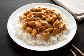 Homemade Orange Chicken with White Rice on a white plate on a black background, side view. Close-up.