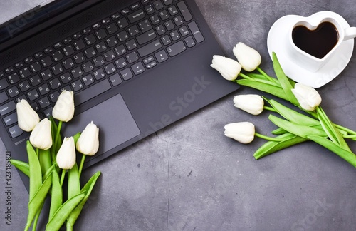 spring concept.  Laptop, notepad, cup of coffee with tulips flowers on gray background. Flat lay. copy space. Workplace. Valentine's day, mother's day, international woman day.