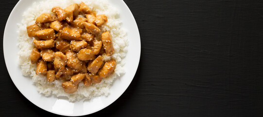 Homemade Orange Chicken with White Rice on a white plate on a black surface, top view. Overhead, from above, flat lay. Copy space.