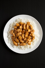 Homemade Orange Chicken with White Rice on a white plate on a black surface, top view. Overhead, from above, flat lay.