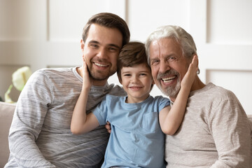 Portrait of happy three generations of Caucasian men sit rest on sofa in living room enjoy family...