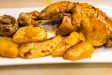 Roast chicken thigh with potatoes and mushrooms on a white plate