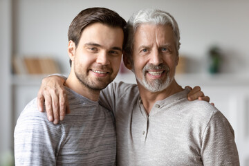 Headshot portrait of happy old 60s grey-haired father and adult grownup son hug pose for family...