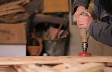 a carpenter in a workshop at work on wood, a man presses strongly with a drill with a round nozzle...