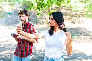 Boyfriend peeks at girlfriend's phone, in the park, jealousy concept.