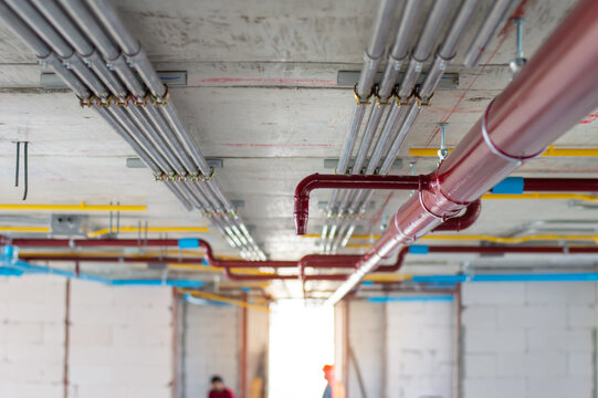 Fire sprinkler system with red pipes is placed to hanging from the ceiling inside of an unfinished new building.Installation of conduits in buildings.Conduit system in building under construction.
