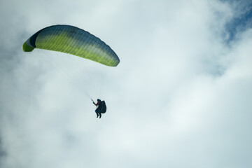 Paraglider flying like a bird in blue cloudy sky.