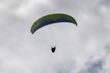 Paraglider flying like a bird in blue cloudy sky.