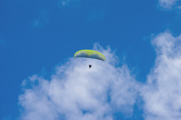 A Paraglider flying into the sky with clouds on a sunny day.