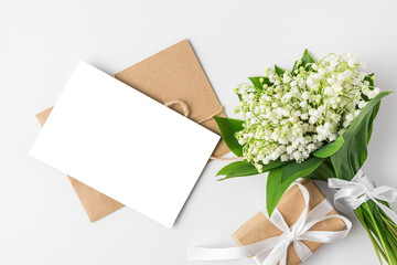 Blank greeting card with spring lily of the valley flowers bouquet and gift box on white background. Flat lay. mock up © samael334