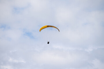 Paraglider flying like a bird in blue cloudy sky.